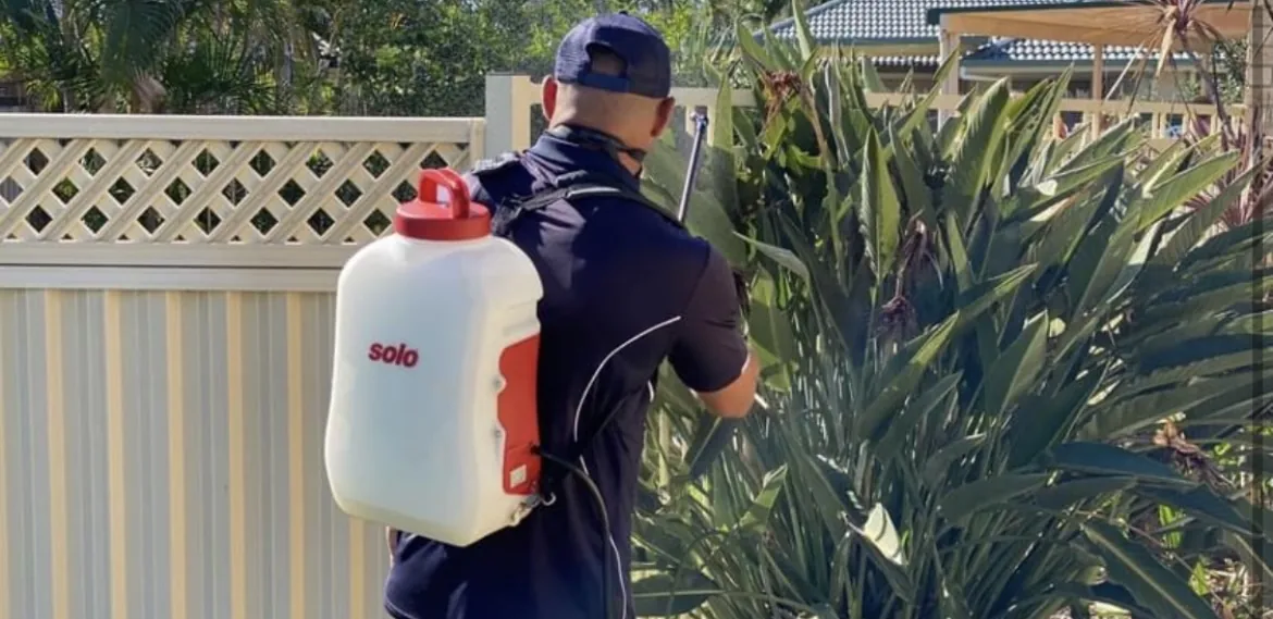 Pest control technician treating an outdoor garden area using a backpack sprayer